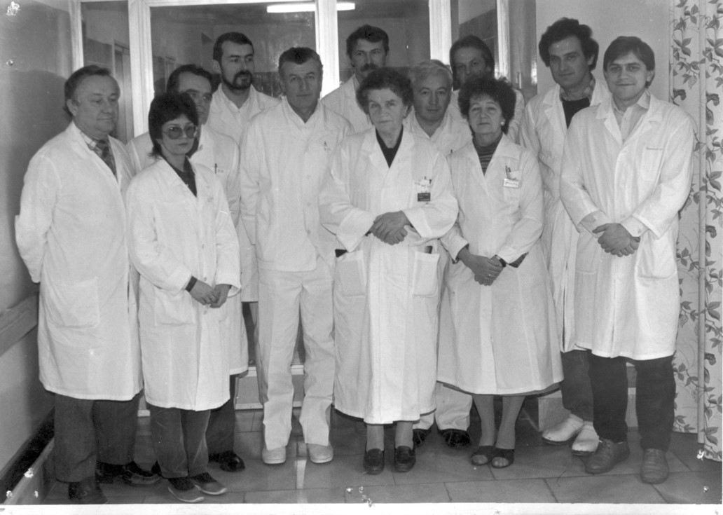 Dwanaście os&oacute;b w fartuchach lekarskich, kobiet i mężczyzn stojących przed szklanymi drzwiami. Zdjęcie czarno-białe